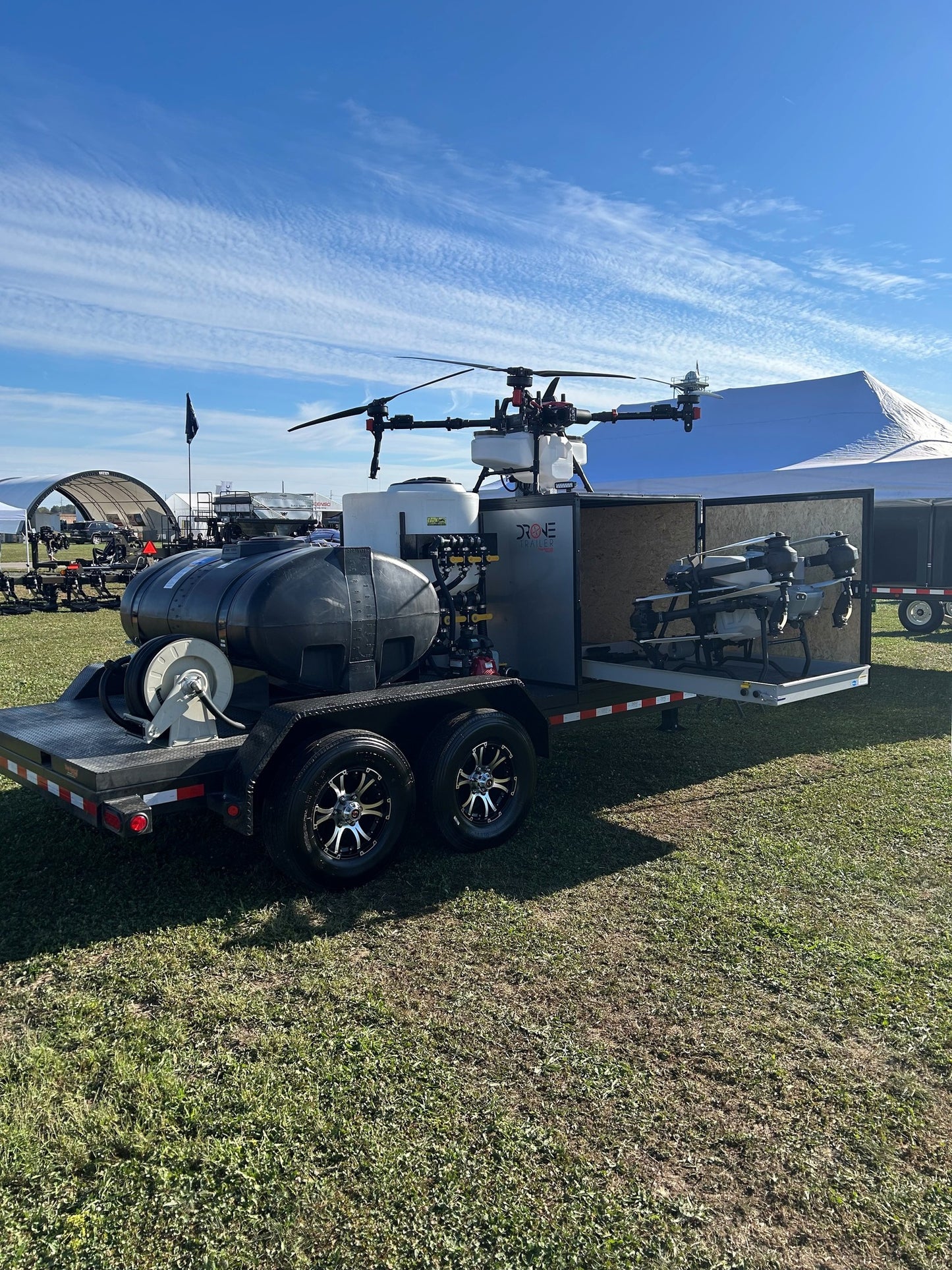 Trailer with a drone and equipment on a grassy field under a blue sky.