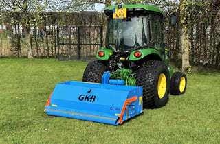Green tractor with a blue attachment labeled GKB on a grassy field.
