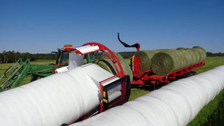A combine of Anderson Wraptor wrapper and trailer attached to a tractor, wrapping a bale of hay.
