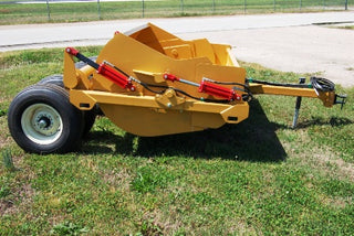 A yellow Durabilt dirt pan with a standard drawbar attached, sitting on grass.