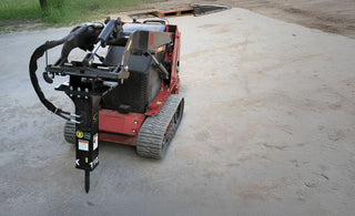 A mini hydraulic breaker attached to a mini skid steer, primarily in red color, designed for demolition tasks.